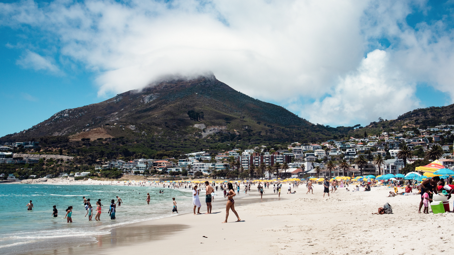 Människor springer mot havet på stranden Camps Bay i Kapstaden. I bakgrunden syns ett berg.